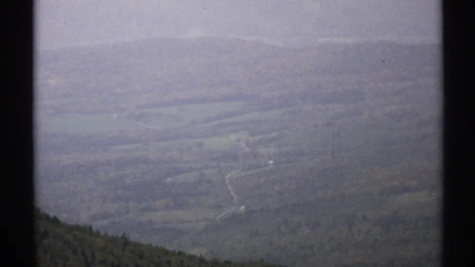1971 Vermont 8mm frame showing a hazy high-angle view over wooded hills and a pale winding road through the landscape.