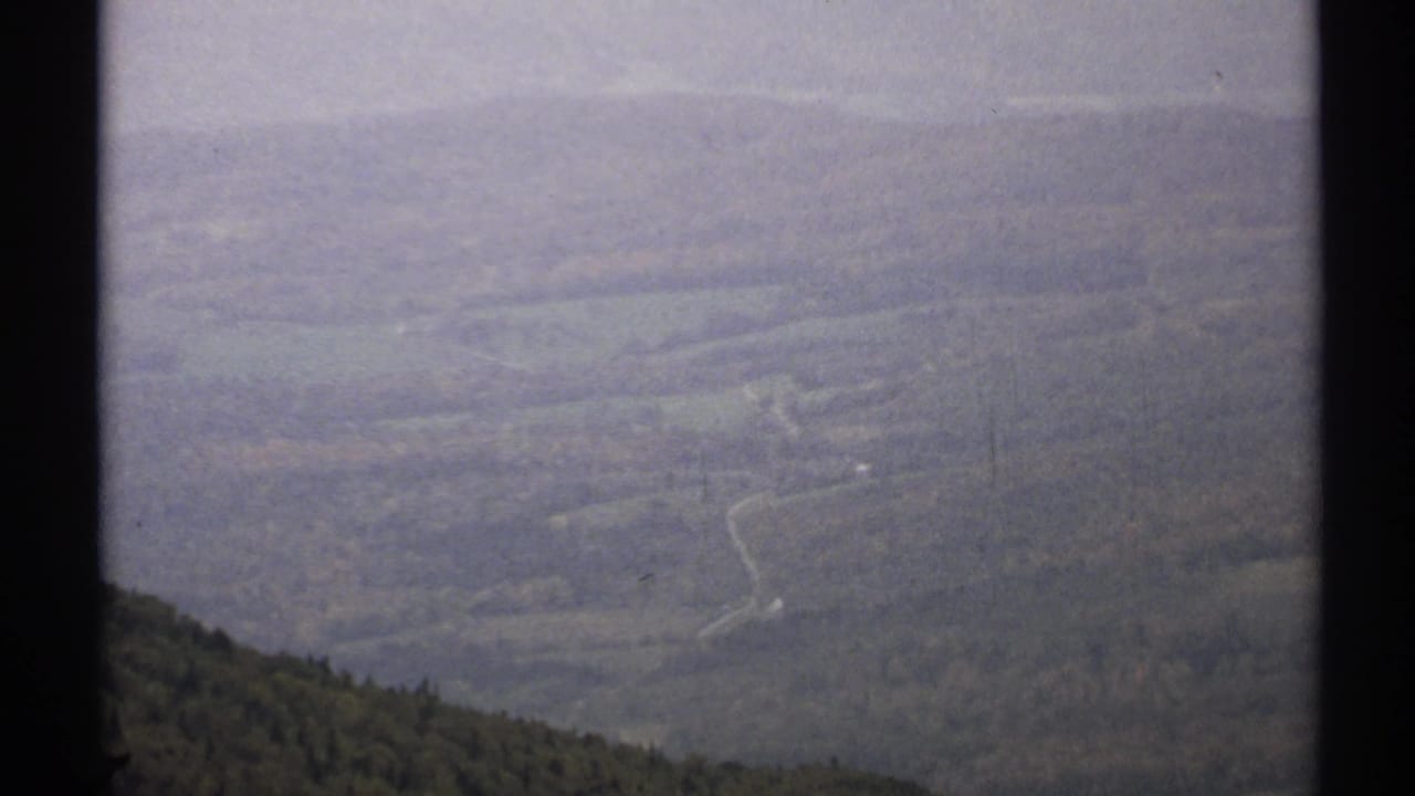 Distant wooded hills and a winding road seen through soft haze.