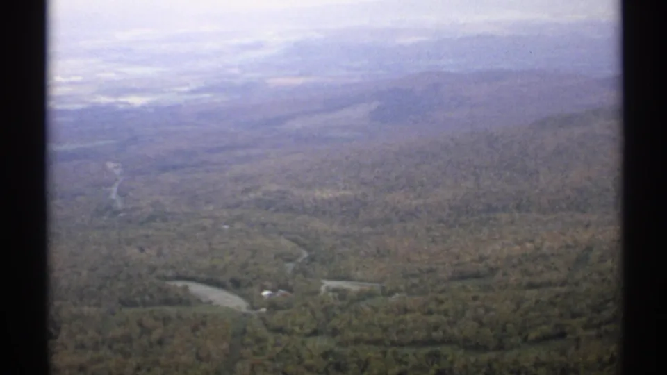 1971 Vermont 8mm frame looking across a broad forested valley with winding river channels and hazy distant hills.