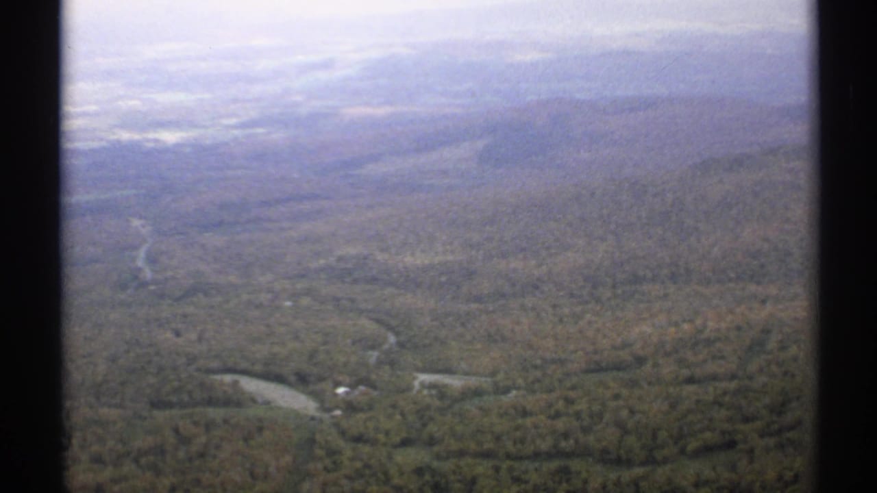 Aerial view of forested hills with winding roads and a small waterway below.