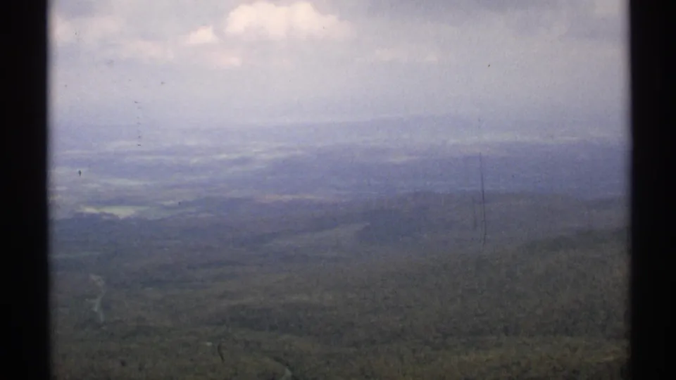 1971 Vermont 8mm frame showing a hazy aerial view across tree-covered hills and a distant valley under a pale sky.