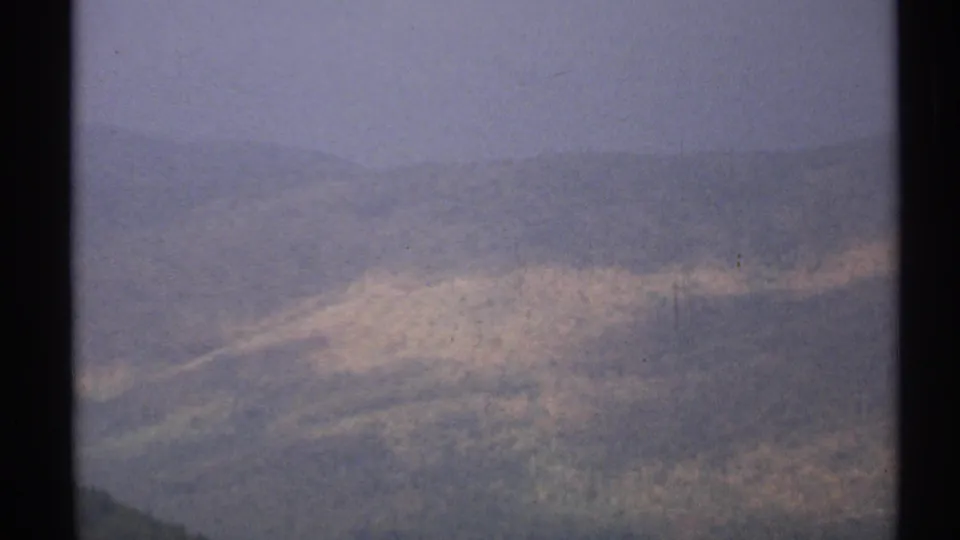 1971 Vermont 8mm frame with wooded hills and pale foliage patches receding into a hazy blue-gray horizon.