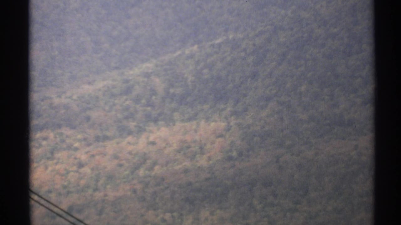 Hazy green mountainside with a dark vertical edge and faint wires crossing the lower left.