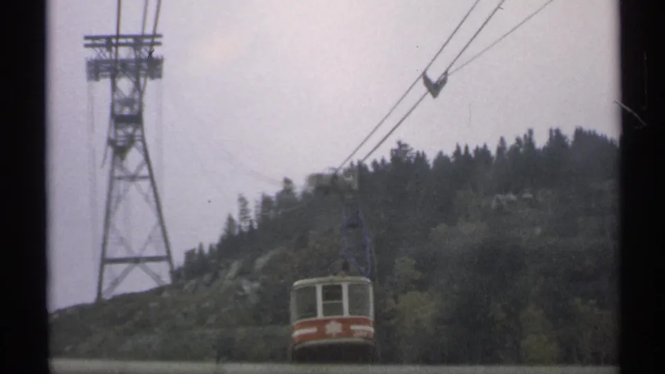 1971 Vermont 8mm frame showing a red-and-white ski lift car passing beneath cables near a tower and forested ridge.