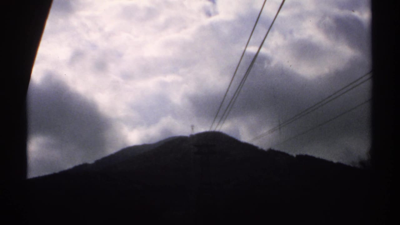 Dark mountain ridge beneath thick clouds with diagonal power lines.
