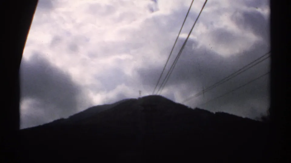 1971 Vermont 8mm frame showing a dark mountain silhouette under heavy clouds, crossed by diagonal utility lines.