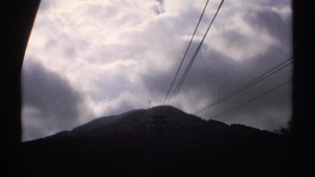 Dark clouds over a silhouetted mountain ridge with power lines crossing the sky.