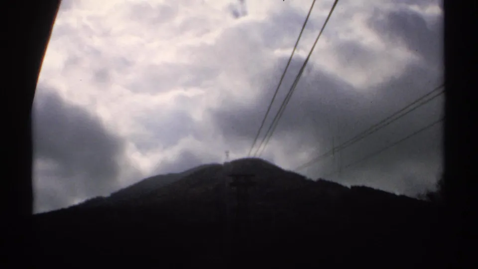 Clouded 1971 Vermont mountain view on 8mm film, with the ridge mostly in silhouette and power lines visible overhead.