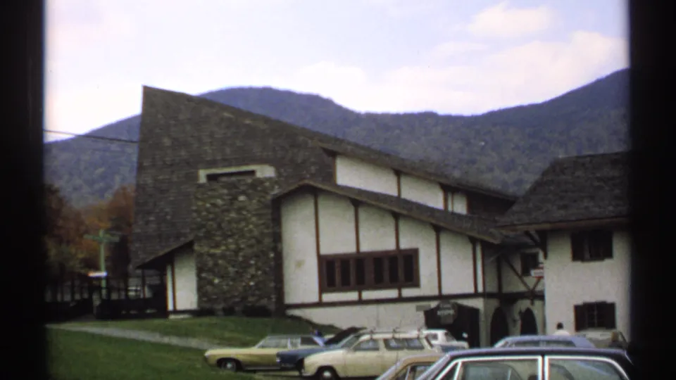 1971 Vermont view of a chalet-style lodge exterior, lawn, parked cars, and wooded mountain backdrop.