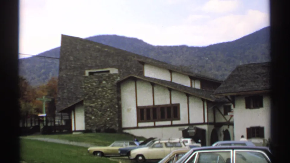 1971 Vermont 8mm frame of a mountain chalet exterior with classic cars parked against forested ridges.