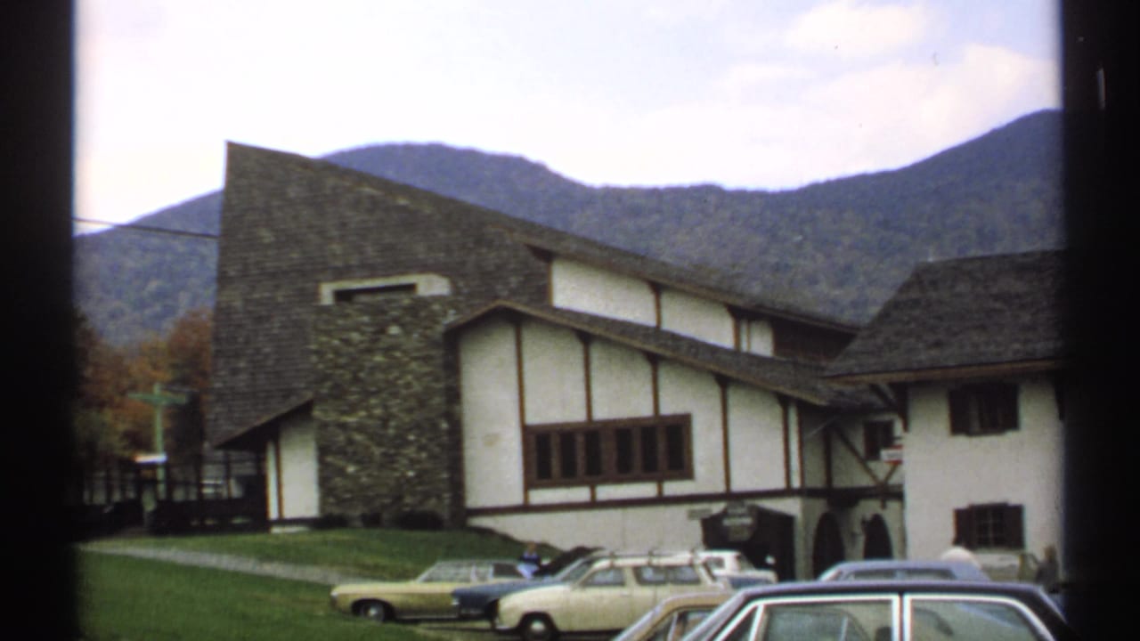 Timber-framed building with parked cars and mountains behind it.