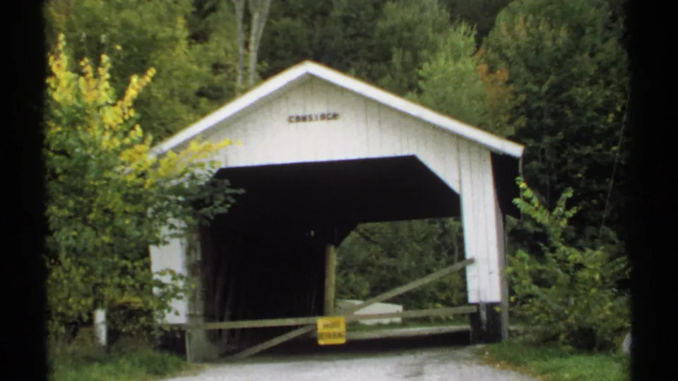 1971 Vermont 8mm frame showing a white covered bridge entrance, roadside barrier, road closed sign, and surrounding autumn trees.