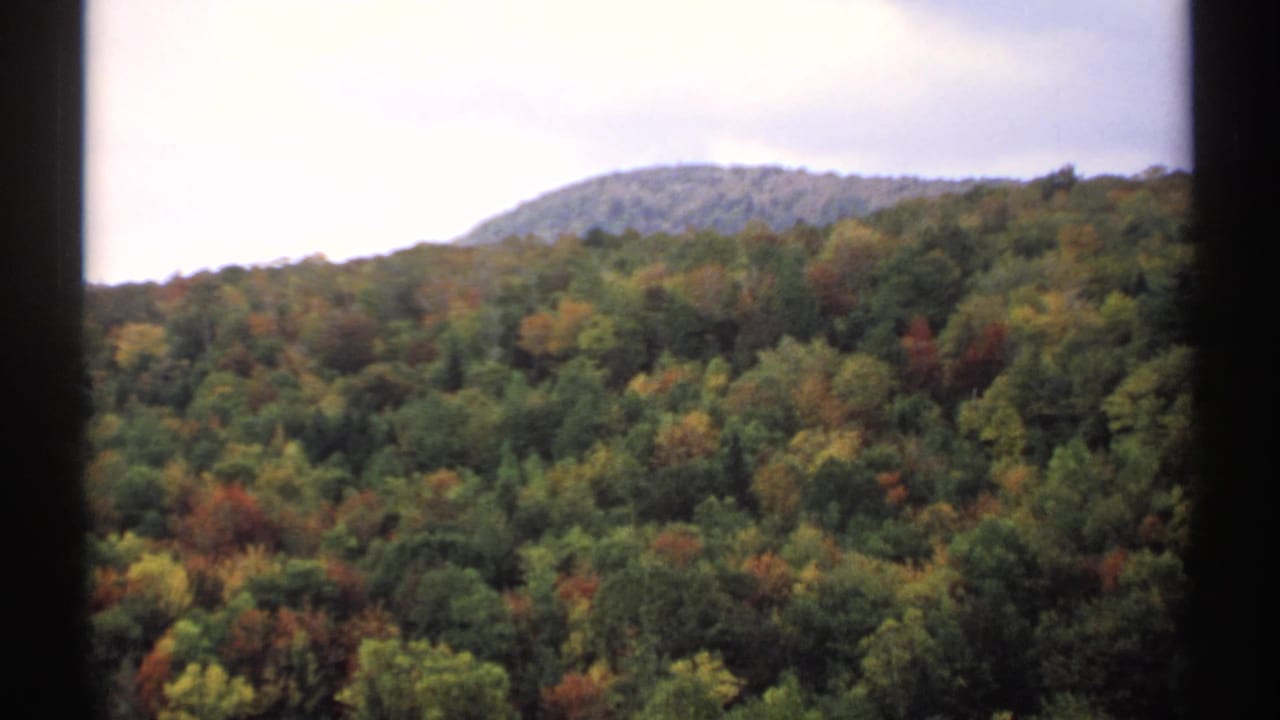 Forested Vermont hills with early autumn color under a pale sky, framed by dark film edges.