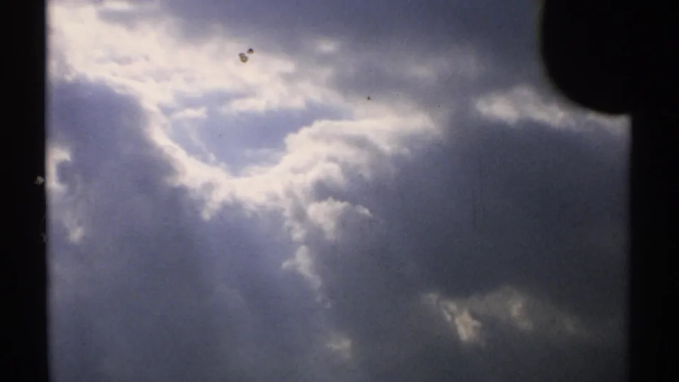 1971 Vermont 8mm frame showing layered clouds, a bright sunlit opening, and visible film dust marks.