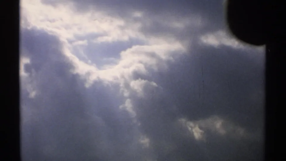1971 Vermont 8mm frame of a cloudy sky with a luminous gap and dark, textured cloud forms below.