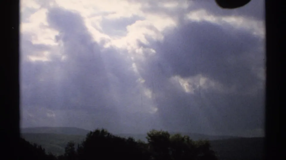 1971 Vermont 8mm frame with dramatic sunbeams cutting through thick clouds above a shadowed rural treeline.