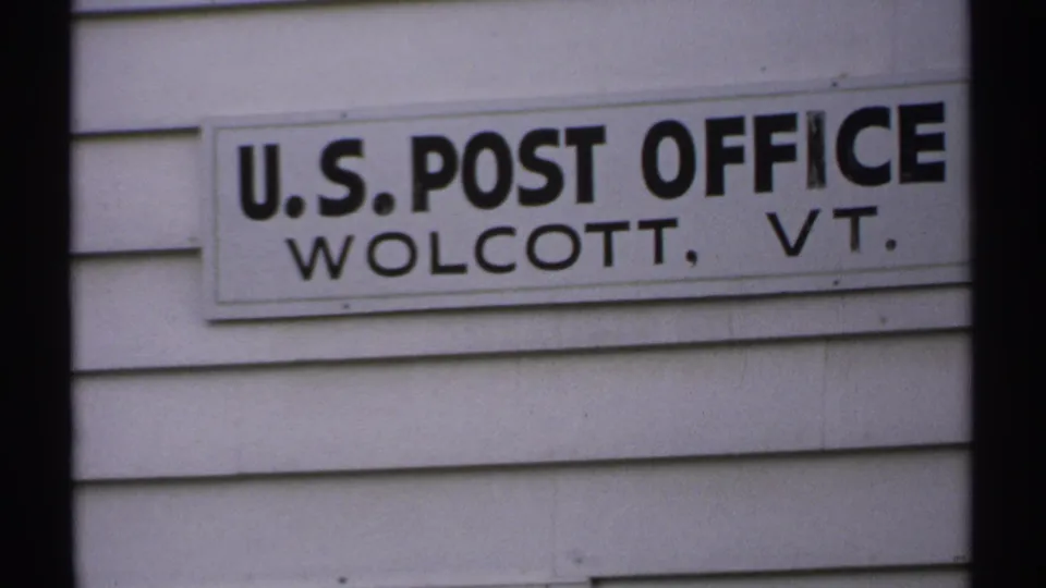 1971 Vermont frame with the U.S. Post Office Wolcott, VT sign and horizontal siding in a tight exterior view.