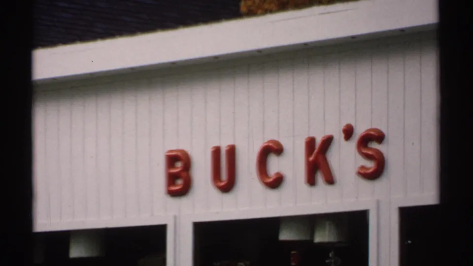1971 Vermont 8mm frame showing red BUCK'S storefront letters, windows, lamps, and white exterior siding.
