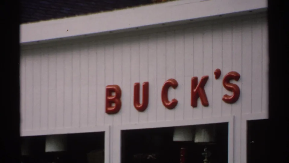 1971 Vermont frame with red BUCK'S lettering above a small storefront, seen from a handheld 8mm perspective.