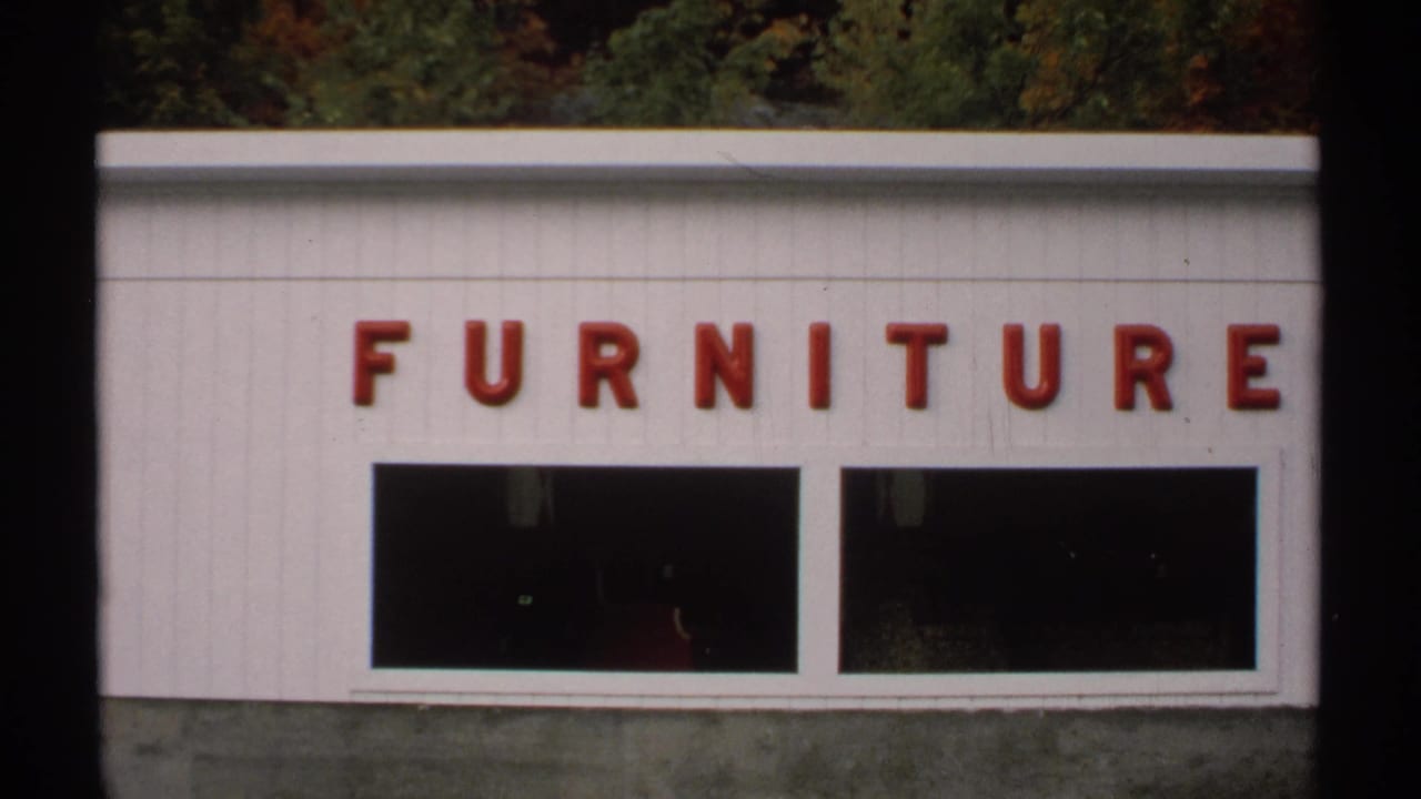 1971 Vermont 8mm frame showing a white furniture store facade with red lettering and dark display windows.
