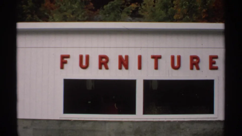 1971 Vermont 8mm frame showing a white furniture store facade with red lettering and dark display windows.