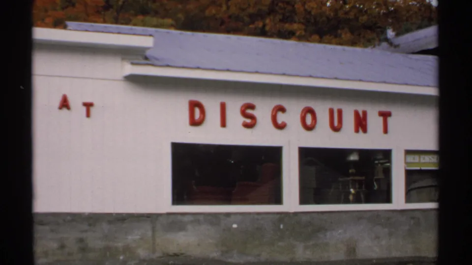 1971 Vermont 8mm frame showing the lower facade with red At Discount lettering and furniture glimpsed through windows.
