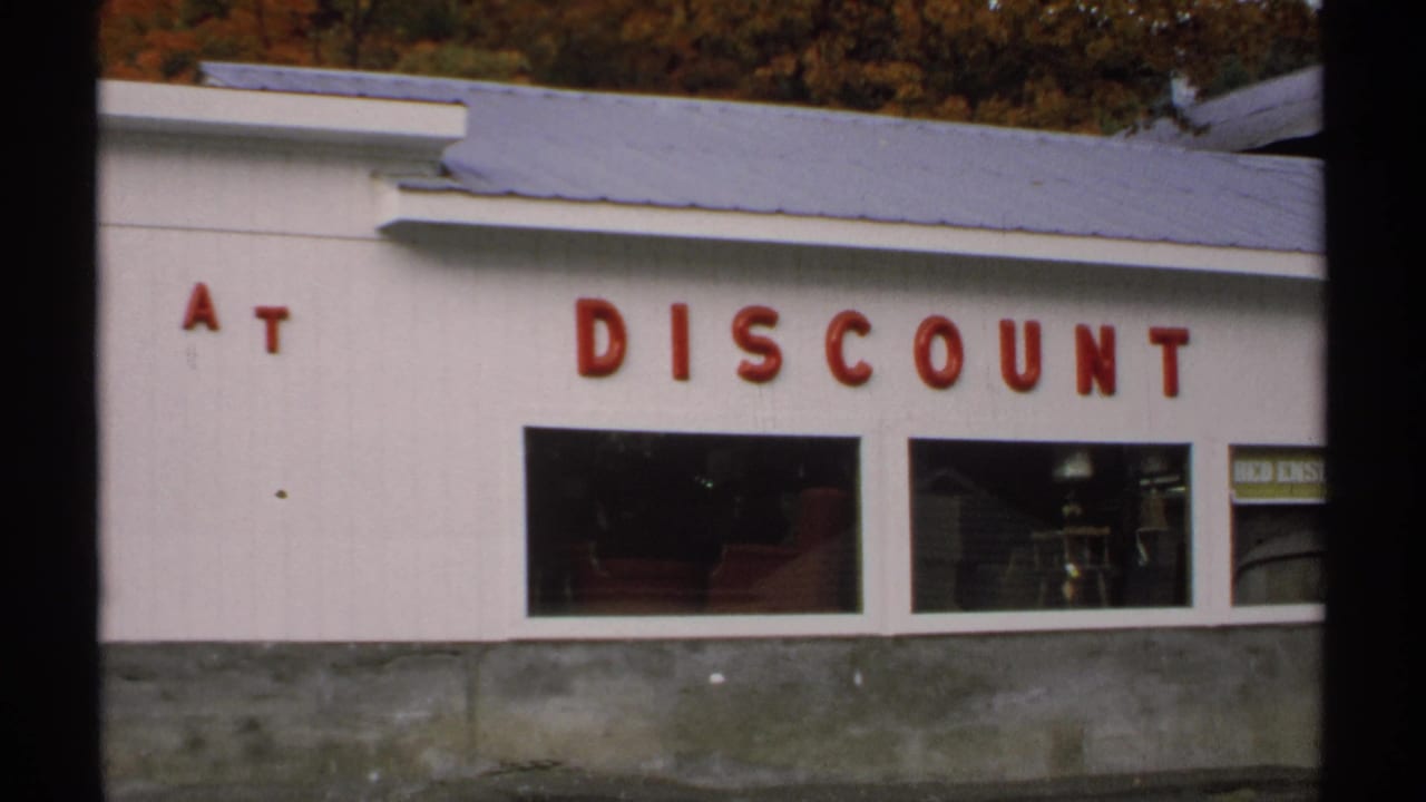 White storefront with red letters spelling part of a discount sign and display windows.