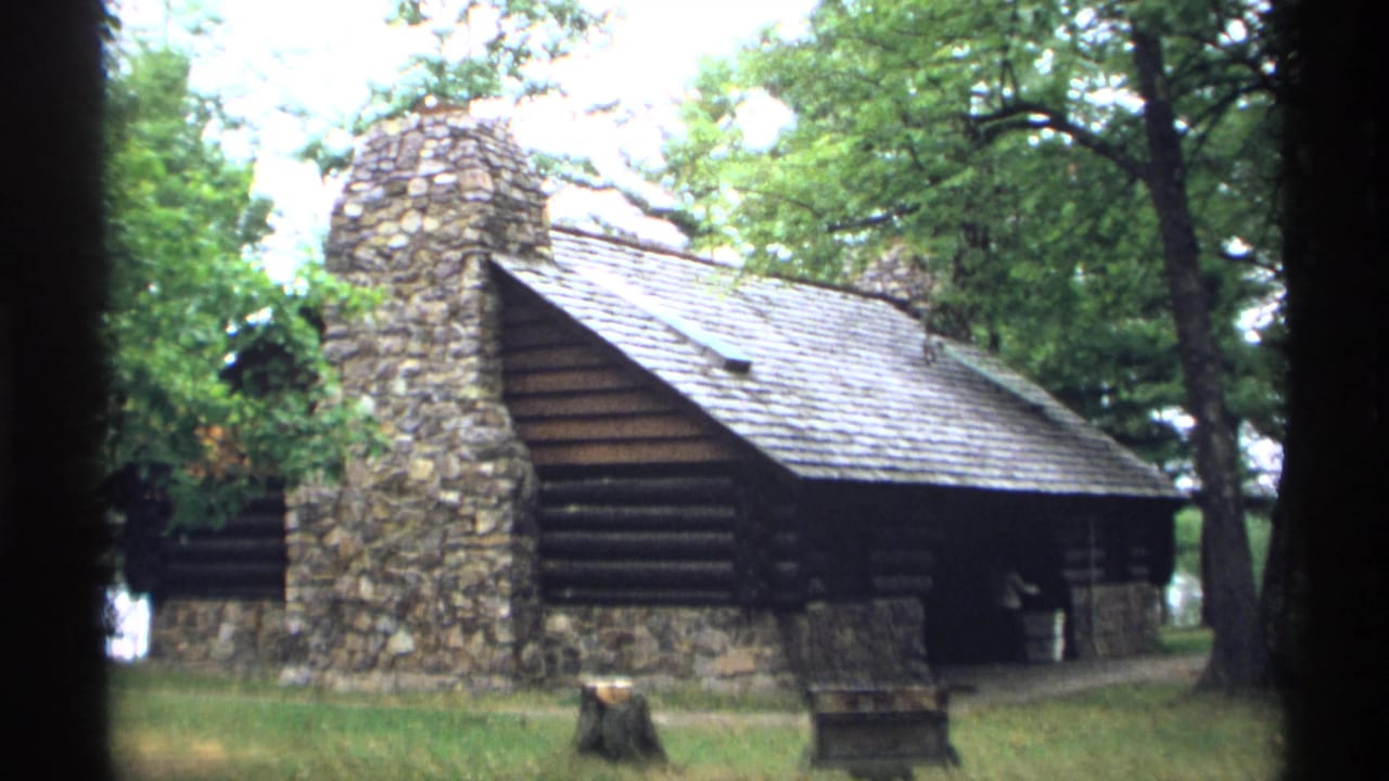Rustic log park building with a stone chimney among trees.