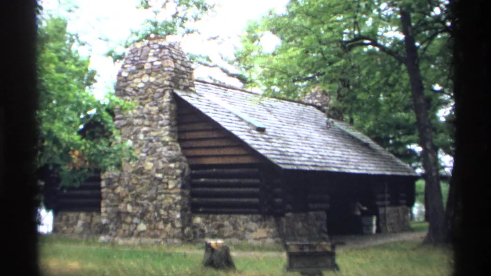 1971 Wisconsin home-movie frame showing a rustic log building with a stone chimney at Brunet Island State Park.