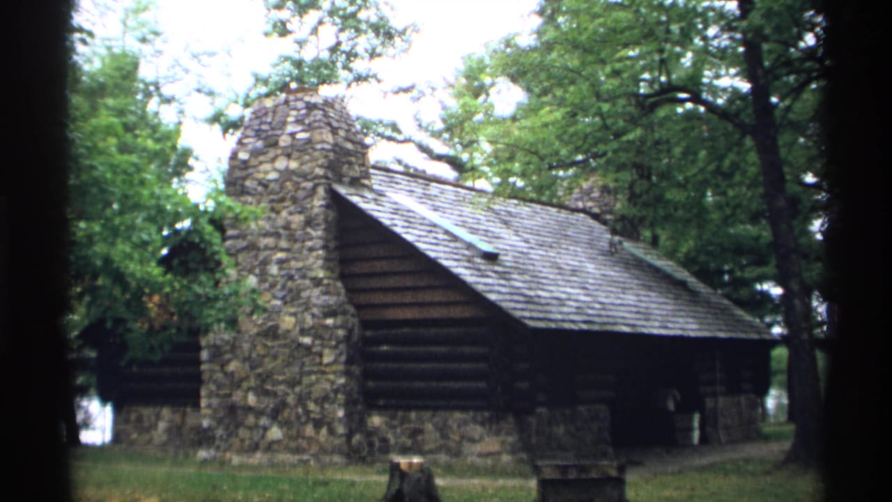 Log building and stone chimney seen through dark film-frame borders.