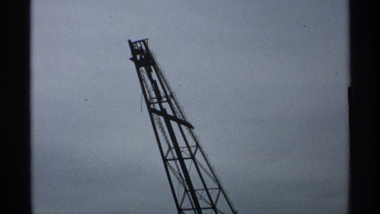 Upper section of a leaning lattice gantry silhouetted against a pale cloudy sky.
