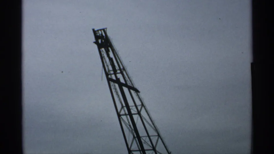 Close 8mm view of the upper portion of a leaning steel gantry against a cloudy Wisconsin sky in 1971.