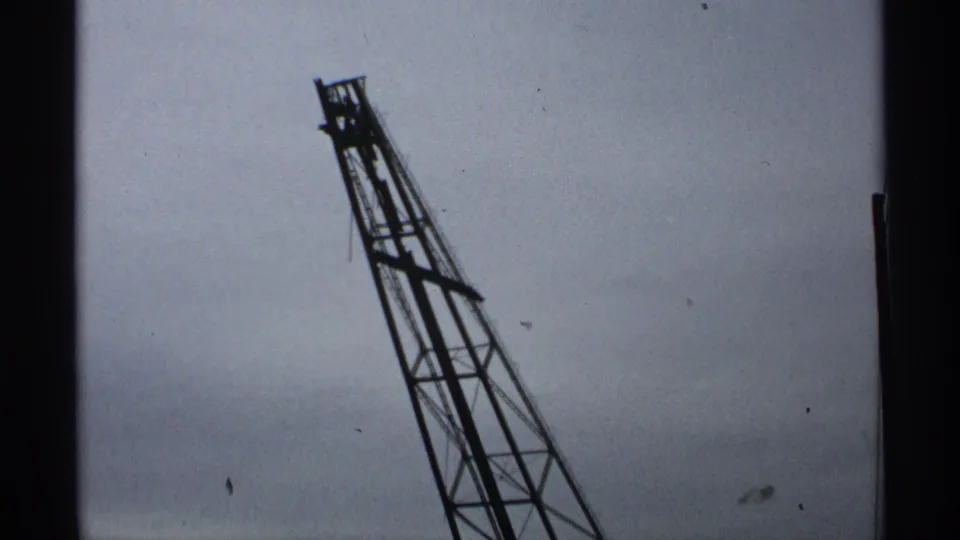 1971 Wisconsin home-movie frame with a tilted gantry boom seen mostly against sky, with visible 8mm grain and scratches.