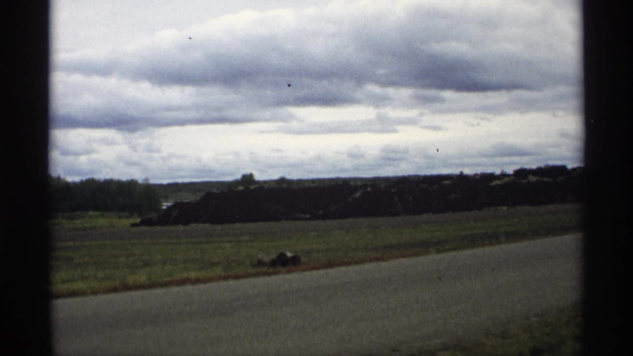 Roadside field with dark pile of material and heavy clouds in the distance.