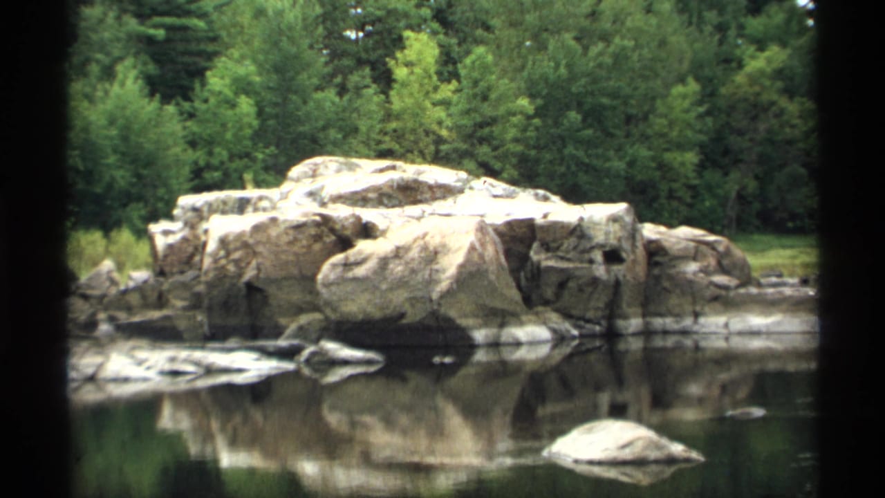 Wide pond view with boulder cluster, trees, and mirrored reflections on the water.