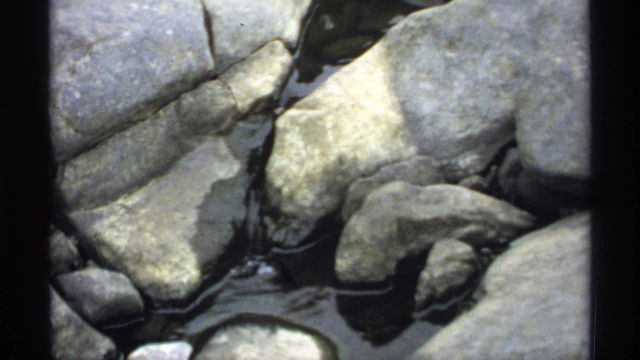 Close 1971 Wisconsin home-movie view of rounded rocks with shallow water moving between them near Jim Falls Dam.