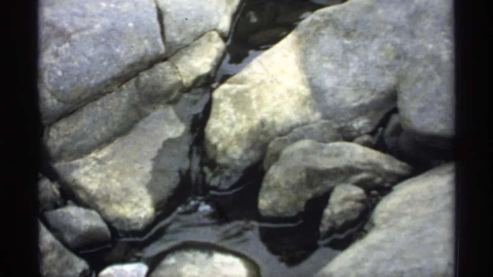 Close 1971 Wisconsin home-movie view of rounded rocks with shallow water moving between them near Jim Falls Dam.