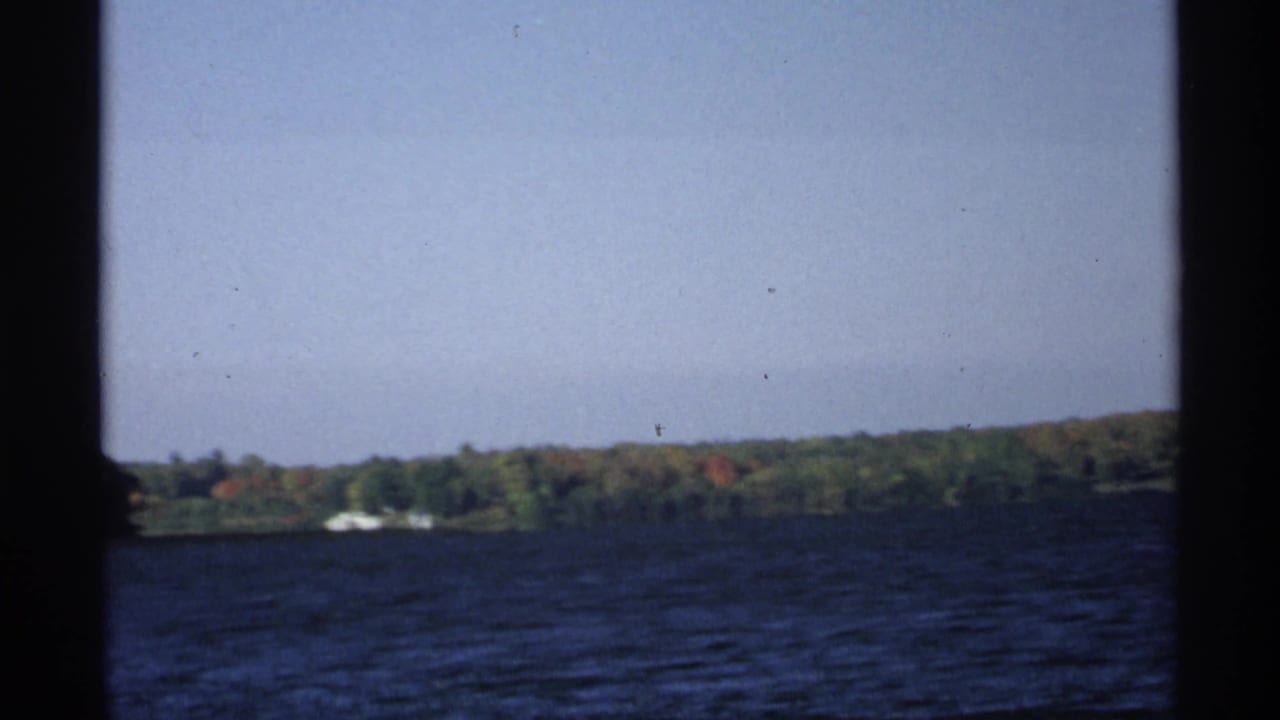 Blue lake water seen through dark frame edges, with a distant tree-lined shore under pale sky.