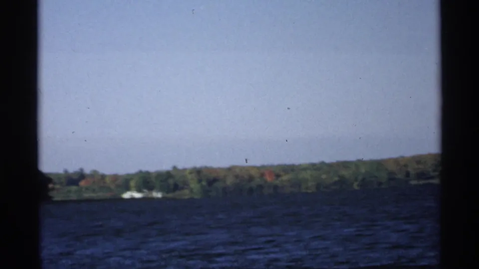 1971 Wisconsin 8mm frame looking across rippled lake water toward a wooded shoreline through dark boat or film-frame edges.
