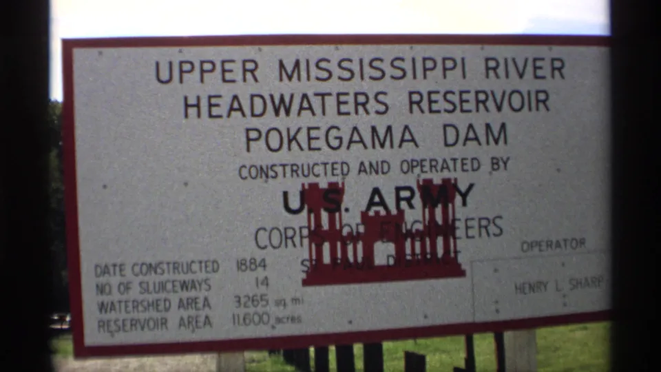 1971 8mm frame of the Pokegama Dam reservoir sign, with technical details visible near the lower left.