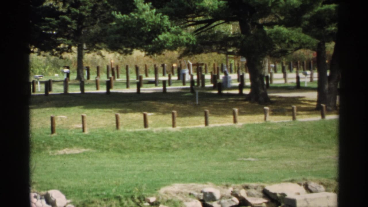 Grassy park with timber posts, paved path, trees, and distant visitors.