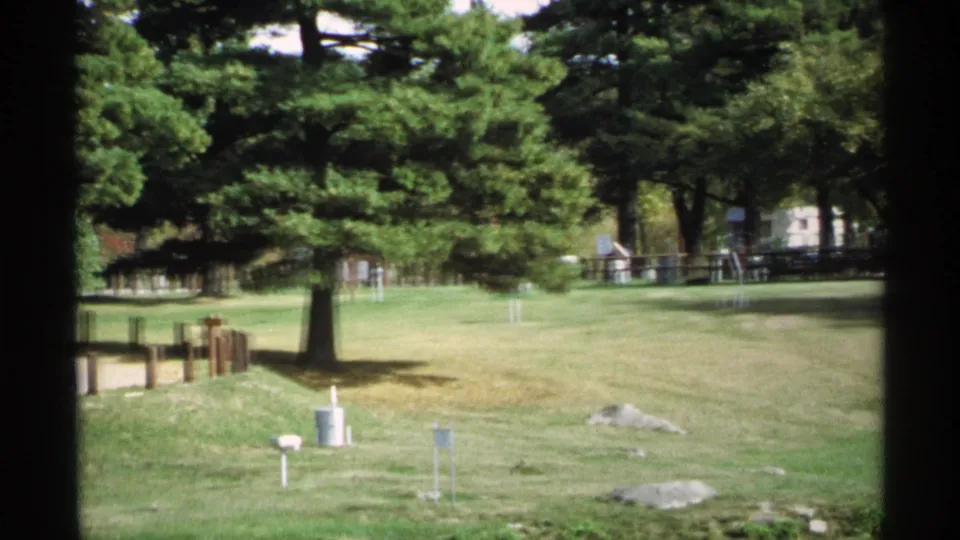 1971 Wisconsin park frame showing open grass, mature trees, scattered rocks, timber posts, and small utility or sign fixtures.