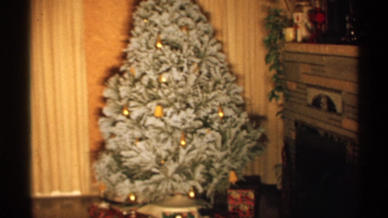 Flocked Christmas tree with warm lights beside curtains and a fireplace.