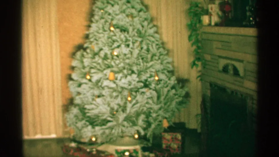 Wisconsin 1971 frame with color-shifted 8mm texture, showing the flocked Christmas tree, lights, fireplace, curtains, and a wrapped gift.