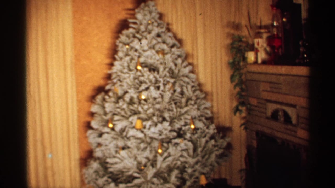 Flocked Christmas tree with warm lights near a fireplace and holiday mantel display.
