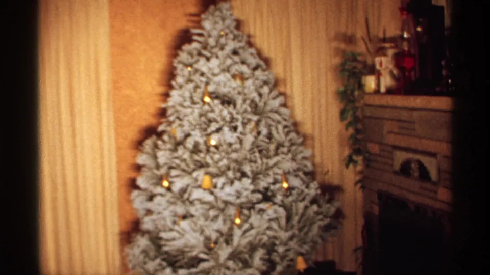 1971 Wisconsin frame of a decorated flocked Christmas tree beside a fireplace, with mantel objects and warm indoor film color.