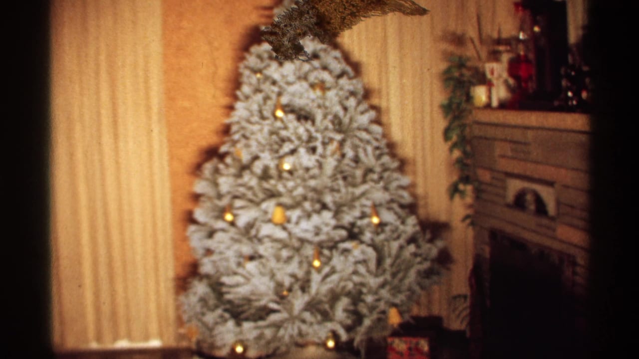 1971 Wisconsin 8mm home-movie frame showing a large white-flocked Christmas tree with glowing lights beside curtains and a fireplace mantel in a private living room.