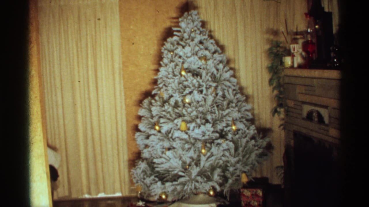 White Christmas tree centered near a fireplace with vertical blinds in the background.