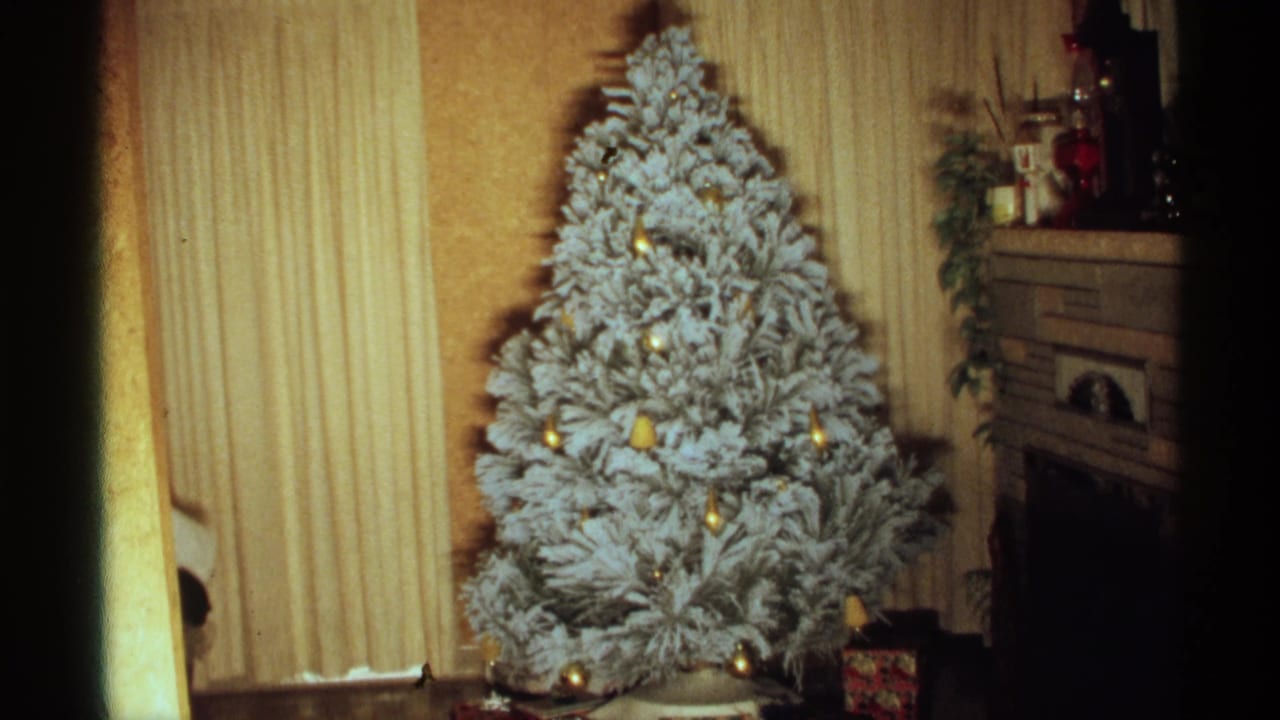 Flocked Christmas tree with gold ornaments beside striped curtains and a fireplace mantel.