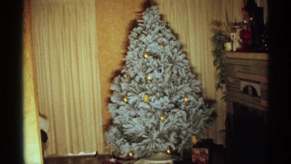 1971 Wisconsin home-movie frame showing a flocked Christmas tree with gold ornaments in a private living room.